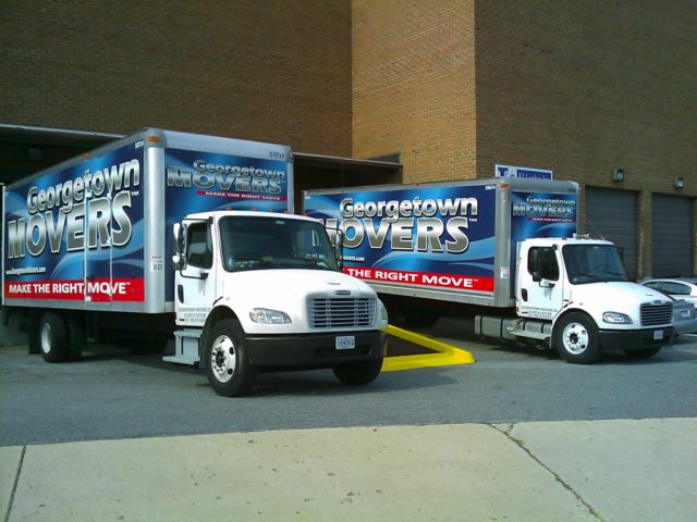 Georgetown Moving & Storage trucks parked next to each other beside a tall brick building.