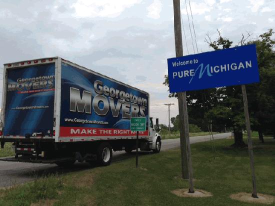 Georgetown Moving and Storage truck on road passing Welcome to Michigan sign.