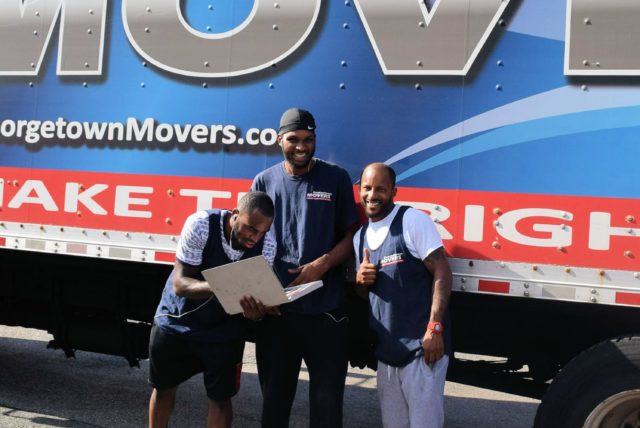 Three Georgetown Moving and Storage employees smiling and standing together in front of a moving truck.