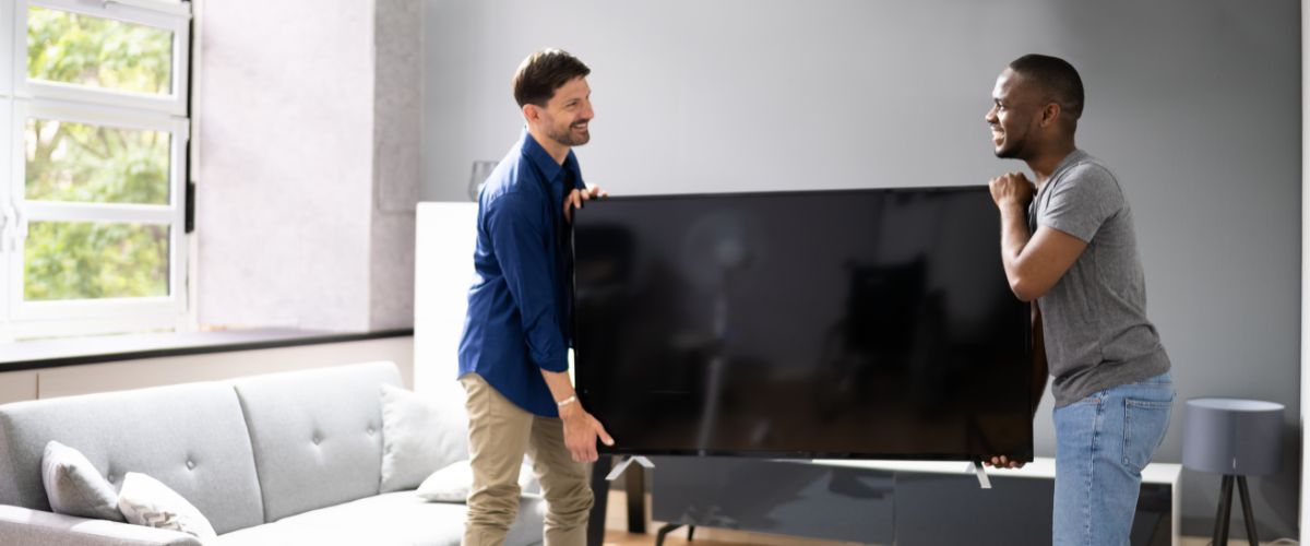 Two people moving a large TV in a living room